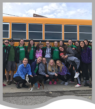 Group of students and a dog pose in front of a school bus